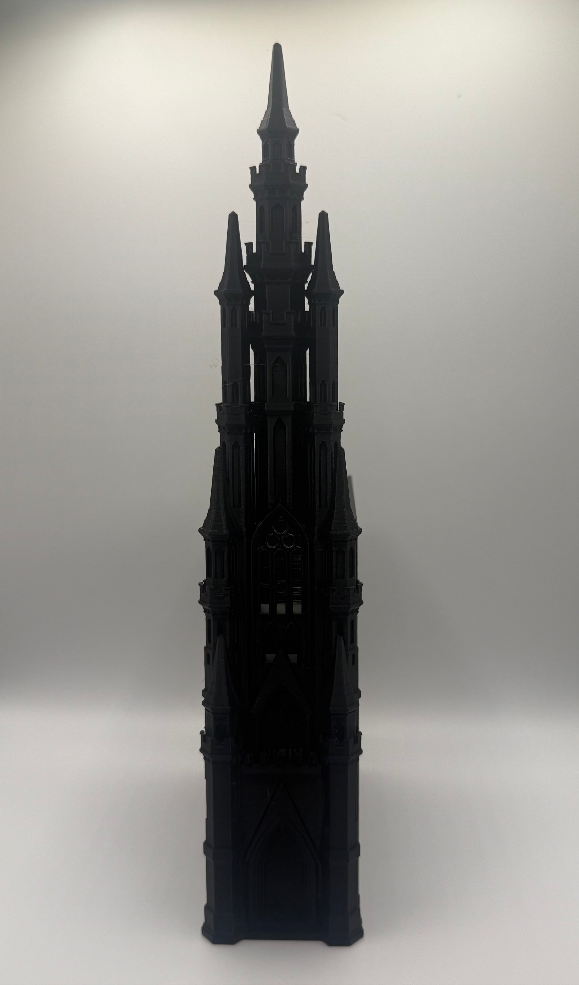A black gothic-style architectural model or miniature tower with pointed spires, photographed against a plain light gray studio background.